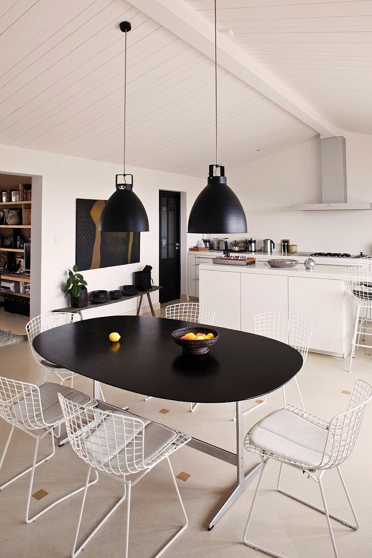 Retro Hängeleuchten über Esstisch mit schwarzer Platte und Stühle aus weißem Metallgestell in funktionaler Küche