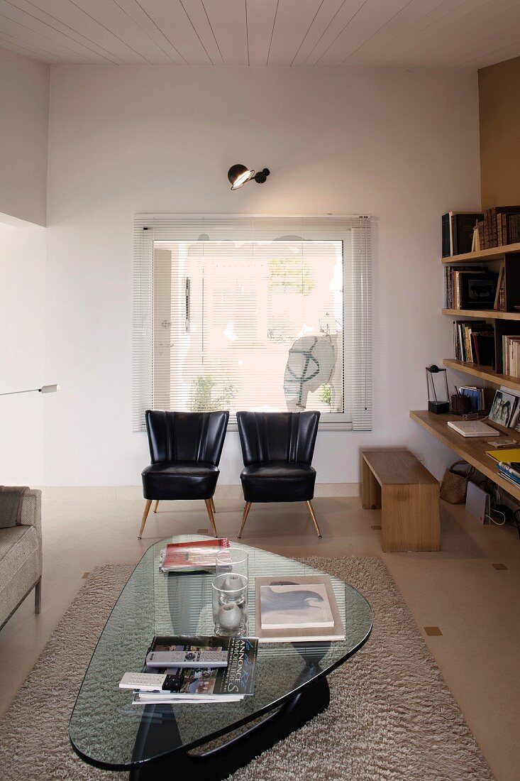 Klassiker Couchtisch mit Glasplatte und Sessel mit schwarzem glänzenden Bezug in schlichtem Wohnzimmer