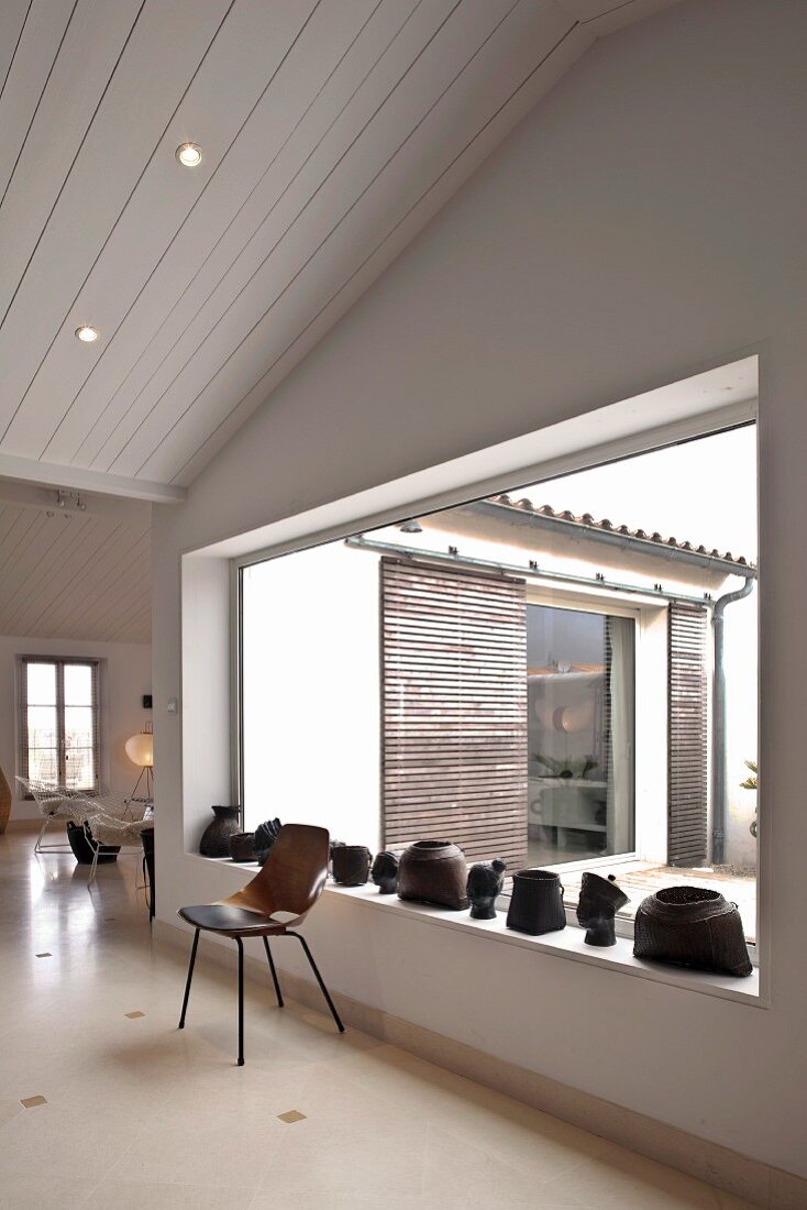 Stuhl aus Holz vor Fenster mit künstlerischen Metallobjekten auf Fensterbank und Blick in Innenhof