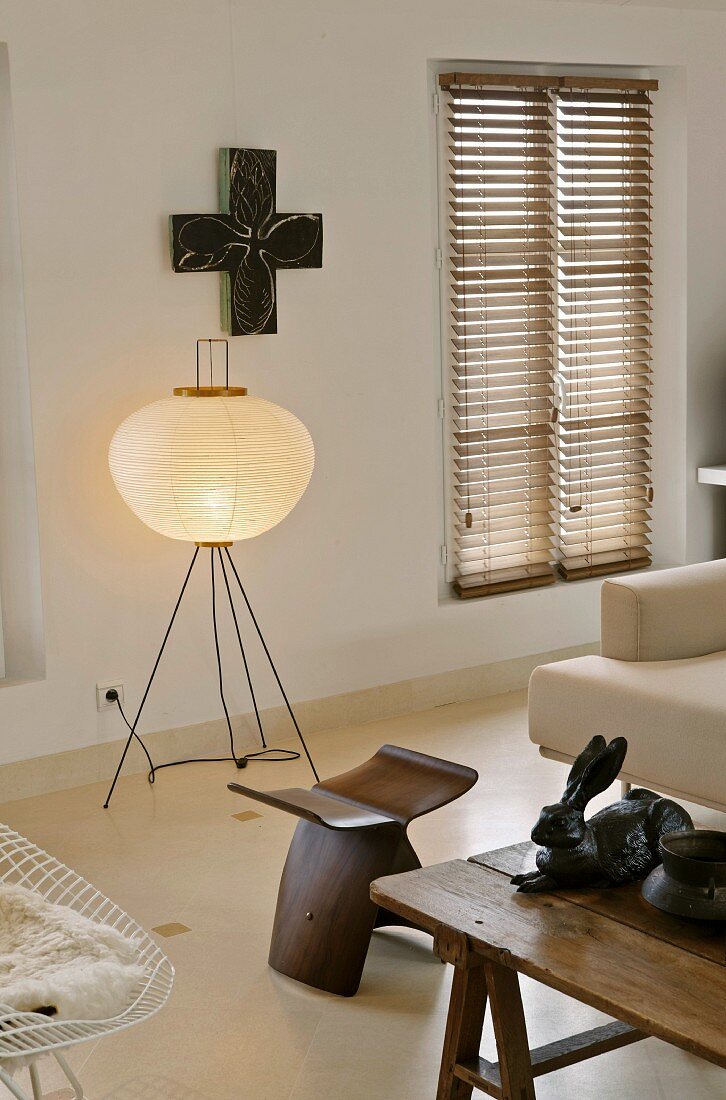 Wohnraum mit Stehlampe und Papierschirm hinter Designerhocker aus Holz
