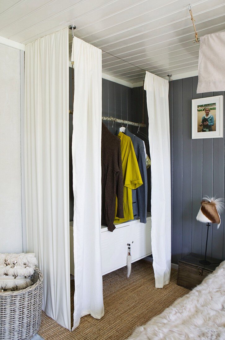 Wardrobe created from clothes rail above white sideboard and screened by curtains in corner of room