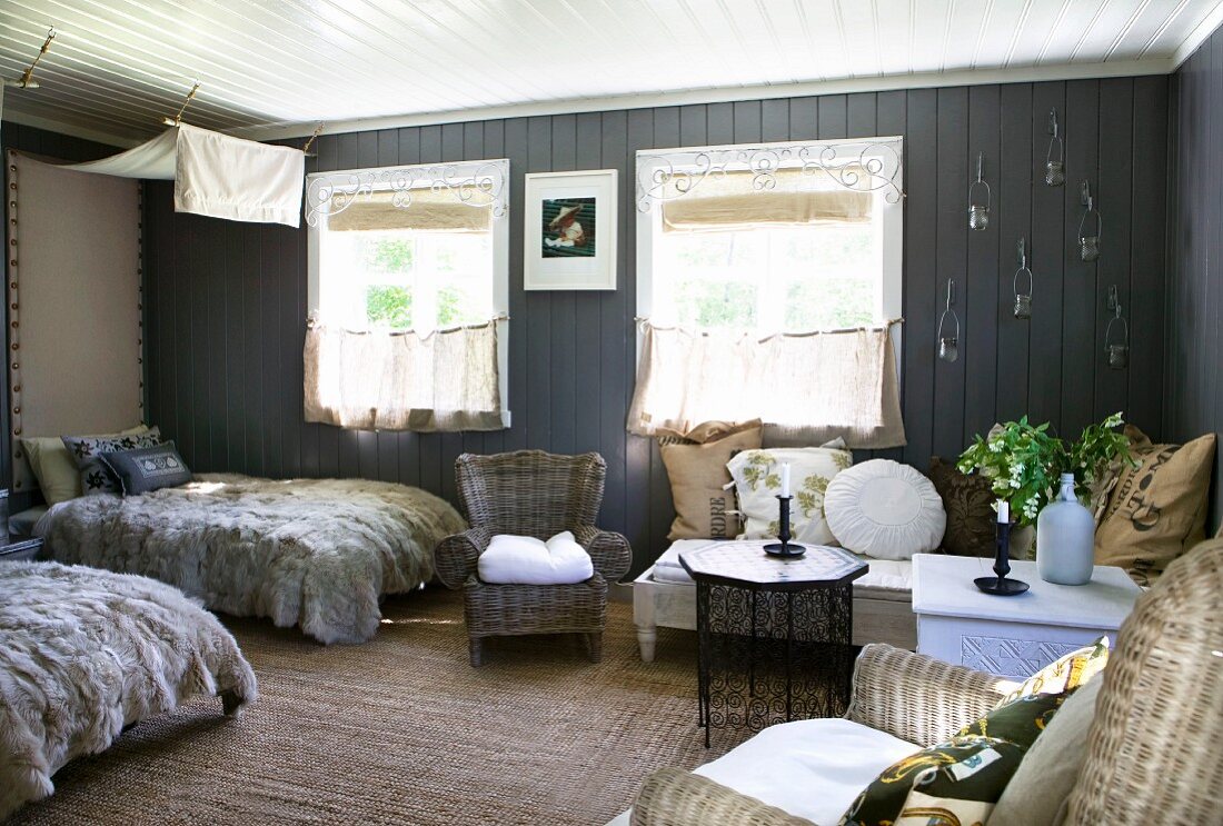 Gemütlicher heller Wohn- und Schlafbereich mit Felldecken auf den Betten und verschiedenen Beistelltischchen, dazu eine Sitzliege mit vielen Kissen und Korbsessel