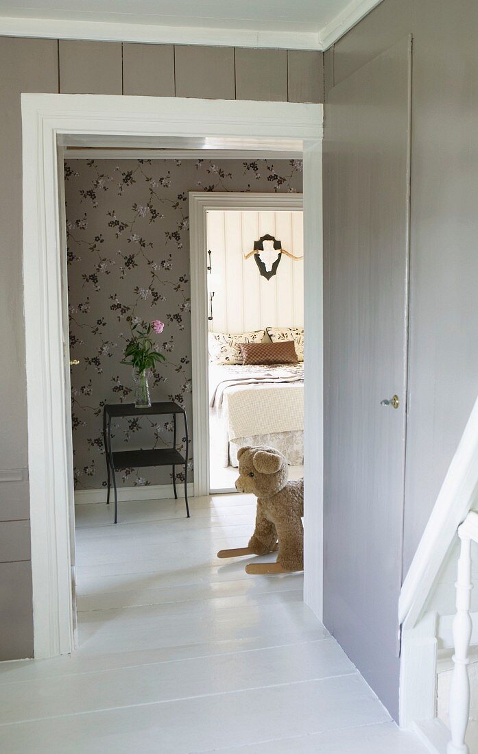 Toys in hallway with floral wallpaper; hunting trophy above large double bed in background