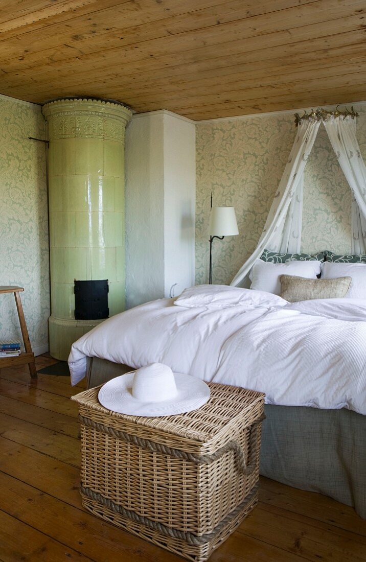Fürstliches Bett mit Baldachin in behaglichem Raum mit viel Holz, grün gemusterter Wandtapete und einem runden Kachelofen in der Zimmerecke