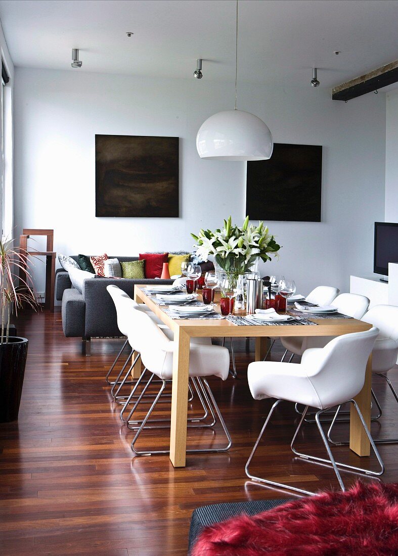 Festively set dining table, white shell chairs and two dark paintings in open-plan loft interior