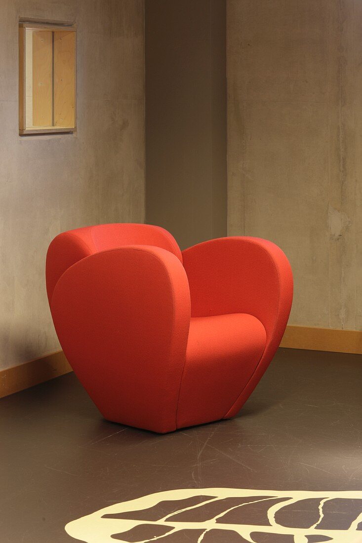 Moderner Sessel in Orange vor Rohbetonwand mit gemustertem Boden (Bibliothek Floriande)