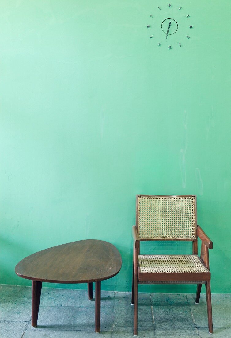 Kidney-shaped table and wooden chair from the 50s in front of a mint green wall with simple relief wall clock (Mill Owner's Association Building)