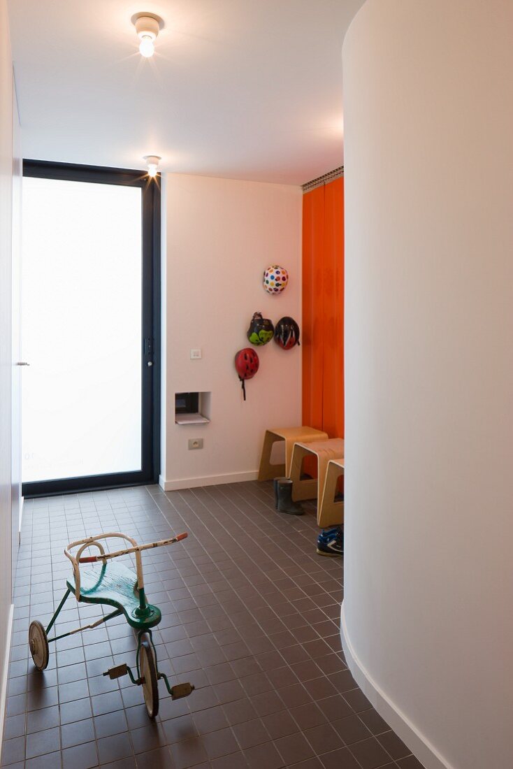 Vintage tricycle in foyer with black tiled floor and modern wooden stools against the wall