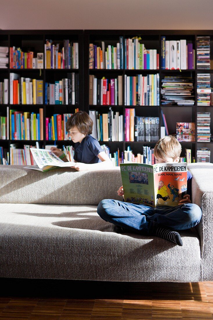 Children reading on comfortable designer couch in front of large bookcase