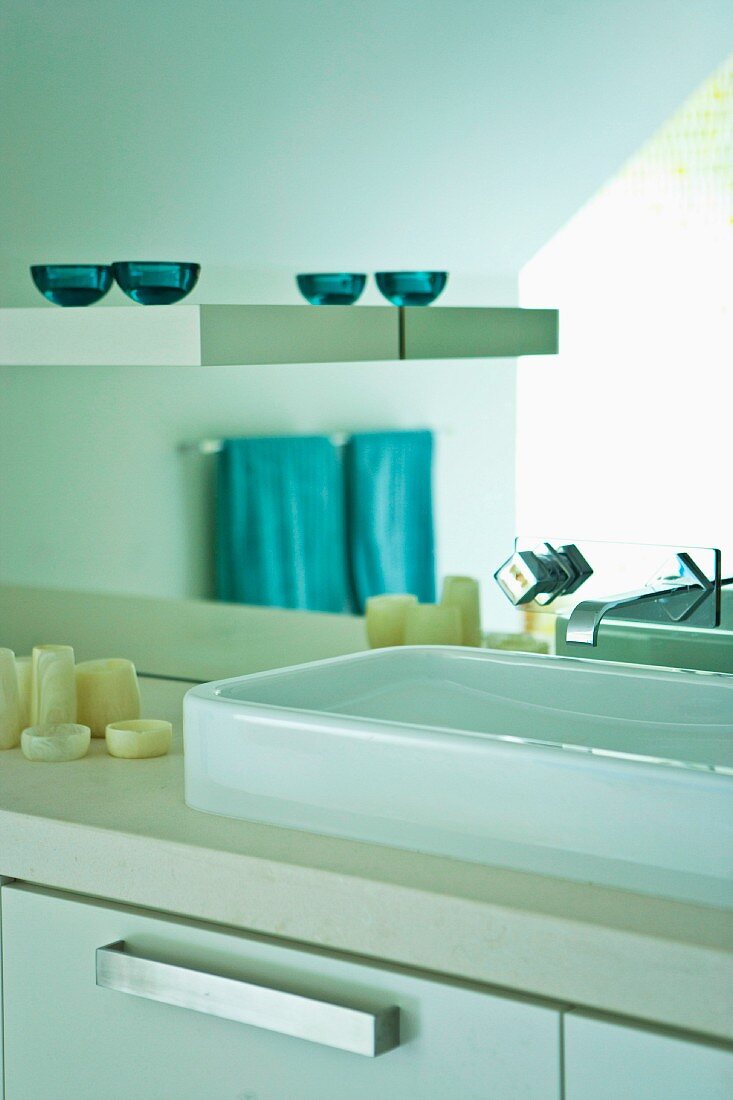 Washstand with counter-top basin below modern, wall-mounted tap fitting and shelf mounted on mirrored wall