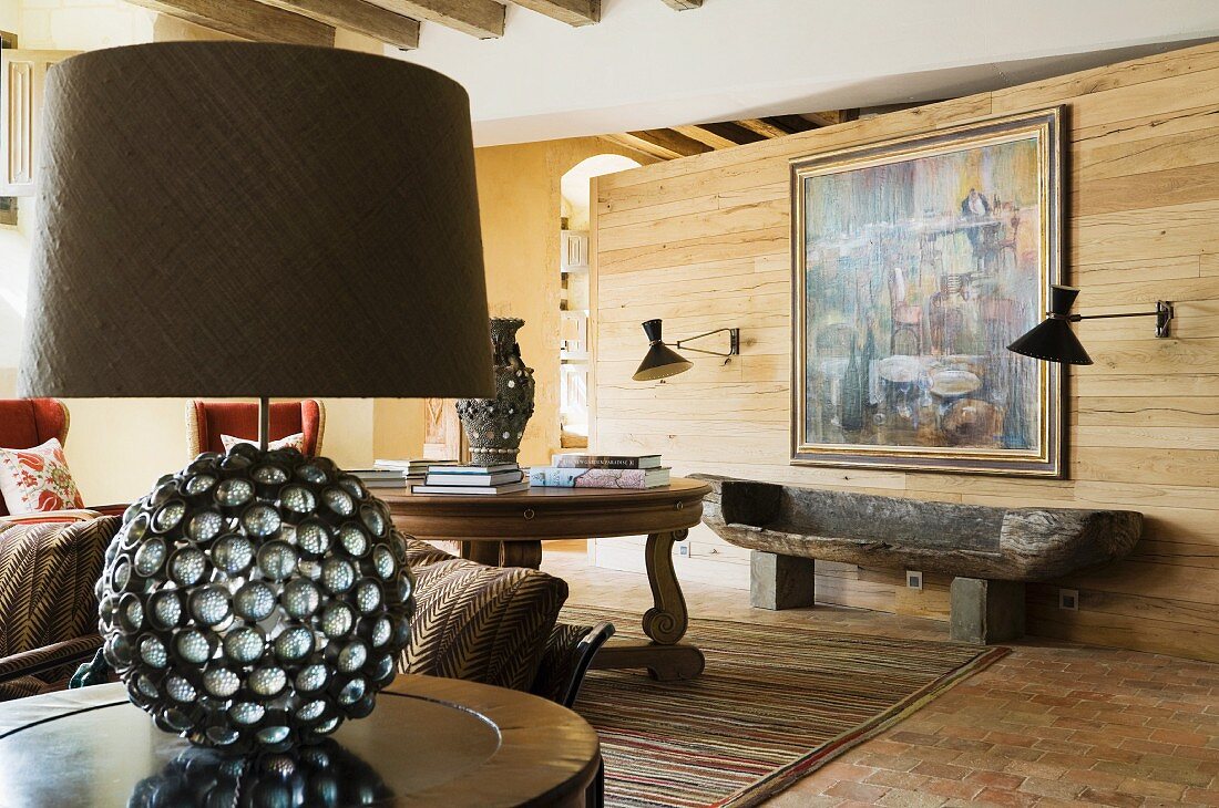 Tischleuchte mit kugelförmigem Fuss auf Beistelltisch in rustikalem Wohnraum mit Holz Raumteiler
