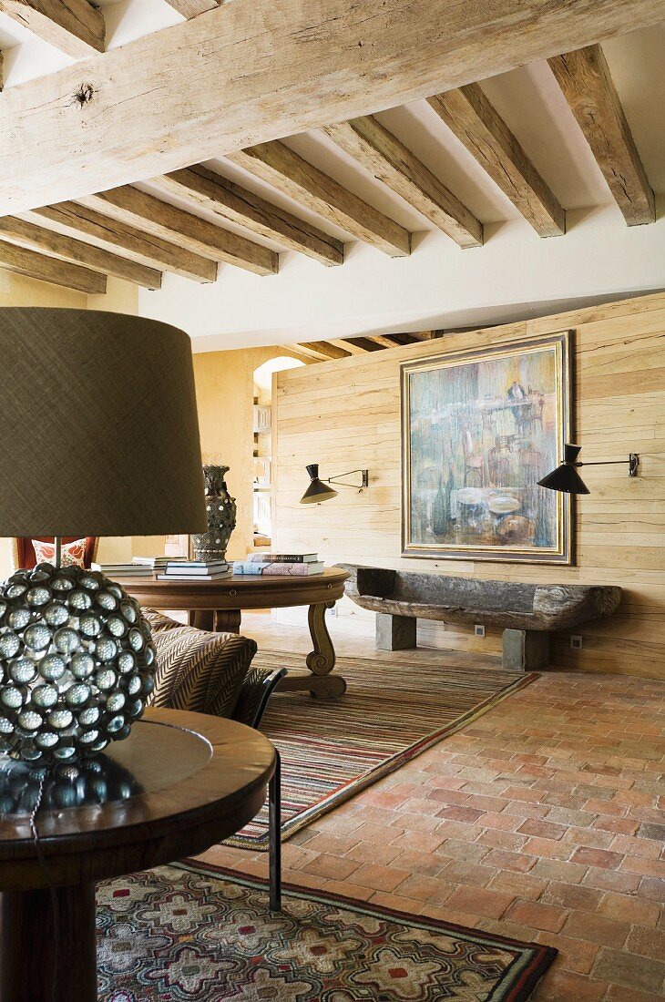Tischleuchte mit kugelförmigem Fuss auf Beistelltisch in rustikalem Wohnraum mit Holzbalkendecke