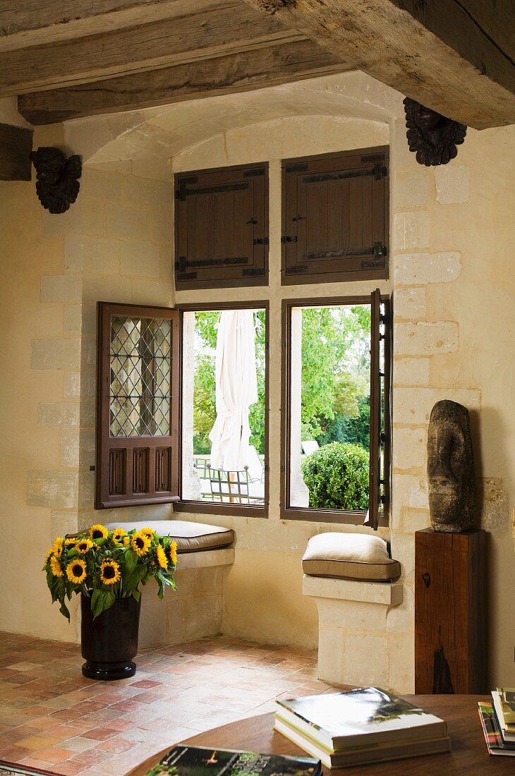 Fensterausschnitt in mediterranem Landhaus - Sonnenbumen in Vase auf Boden vor offenem Fenster mit Gartenblick