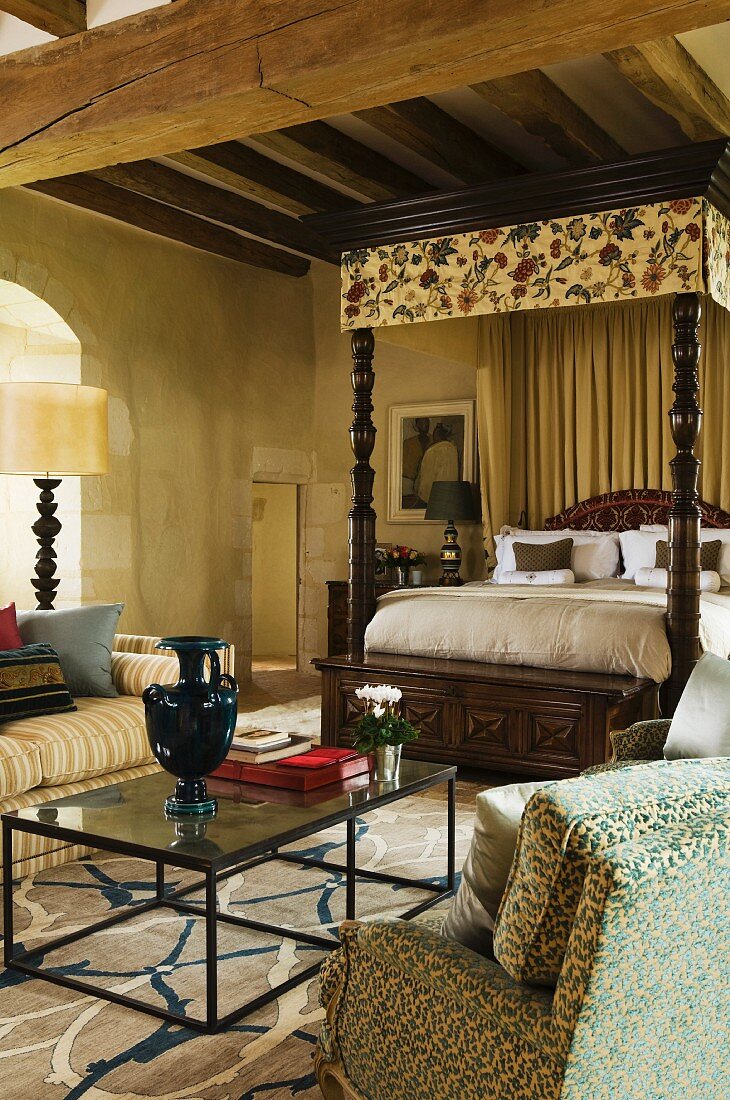 Seating and modern coffee table in front of traditional four-poster bed with canopy