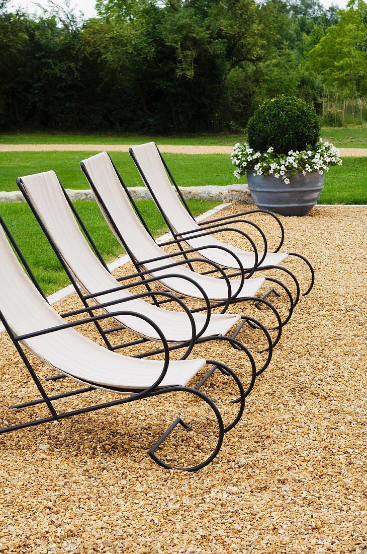 Elegante Liegestühle mit schwarzem Metallgestell und Segeltuch auf Kiesboden im Garten