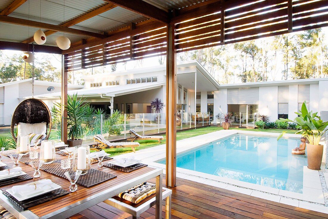 Überdachter Terrasse mit Esstisch und Blick auf Pool und eingeschossiges luxuriöses weißes Pultdachhaus