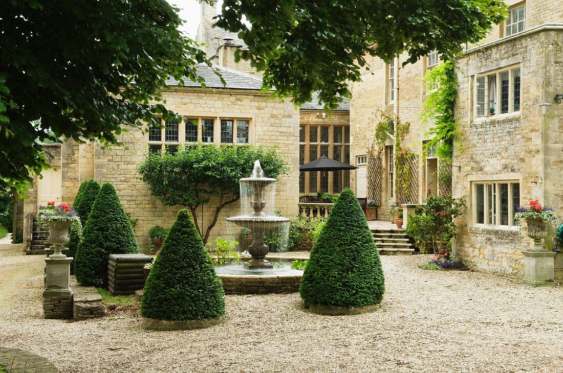 Kegelförmige Büsche um Springbrunnen im Innenhof eines englischen Schlosses