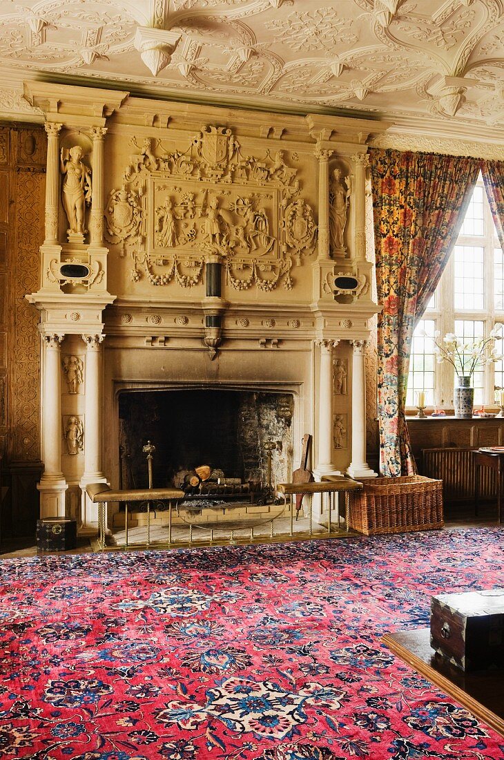Patterned rug in front of grandiose fireplace with carved stone garlands and sculptures in grand salon