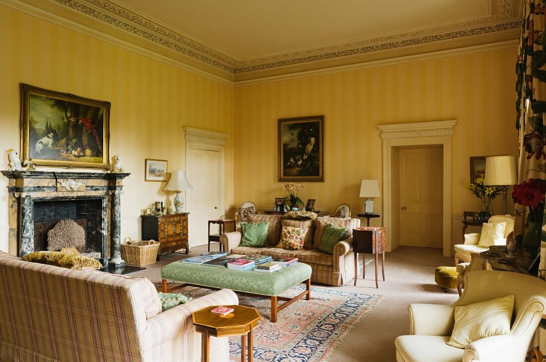 Herrschaftlicher Salon mit gelb gestreiften Wänden und schlichte Sofagarnitur vor offenem Kamin mit ländlichem Flair