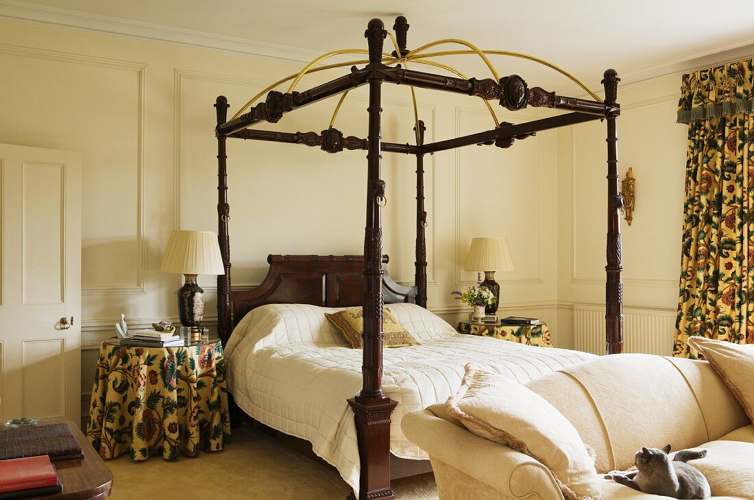 Doppelbett mit Holzgestell und Säulen neben Nachttisch mit geblümter Tischdecke, passsend zum Vorhang in herrschaftlichem Schlafzimmer