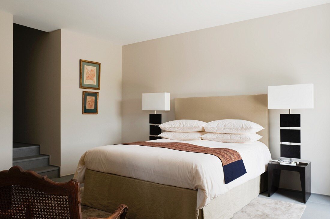 Elegant bedroom with headboard flanked by designer bedside lamps against pale grey wall