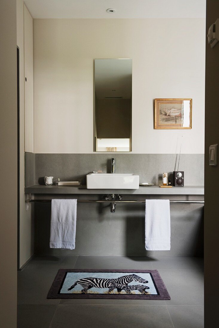 Blick durch offene Tür auf minimalistische Waschtischzeile vor halbhoher, hellgrauer Wand in schlichtem Bad