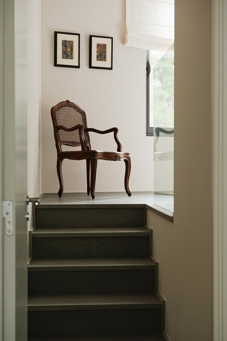 Blick durch offene Tür auf antiken Stuhl mit Geflecht in Rückenlehne auf Podest mit Treppe