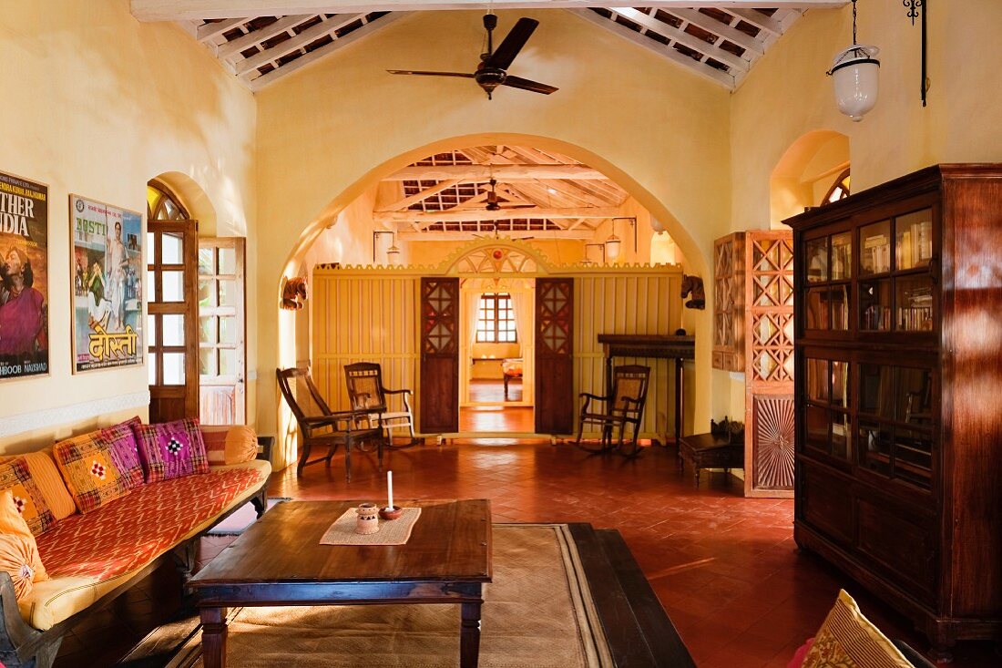 Gelb getönter, indischer Wohnraum mit schlichter Sitzbank und Couchtisch vor breitem Durchgang mit Rundbogen