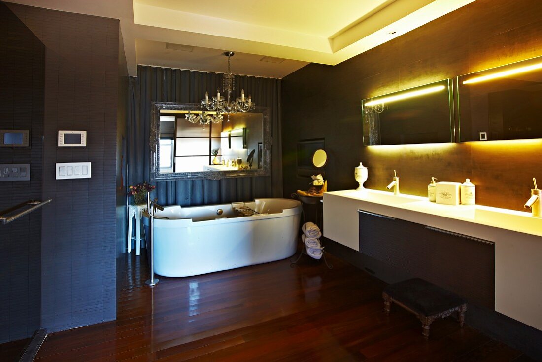 Klassisch elegantes Bad mit indirekter Spiegelbeleuchtung über dem langen Waschtisch und Kronleuchter über der Wanne