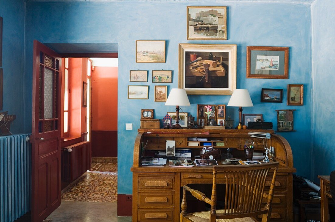 19C wooden desk in blue painted study with assorted oil and water colour artworks on wall