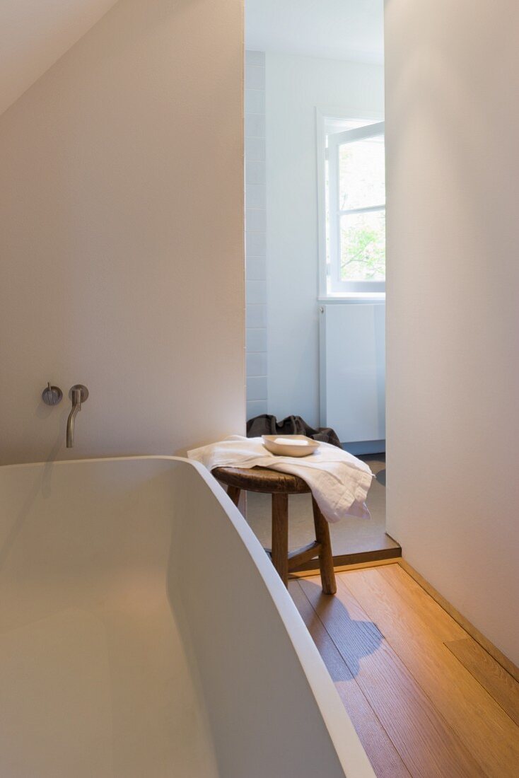 Holzschemel neben moderner Badewanne in minimalistischem Bad