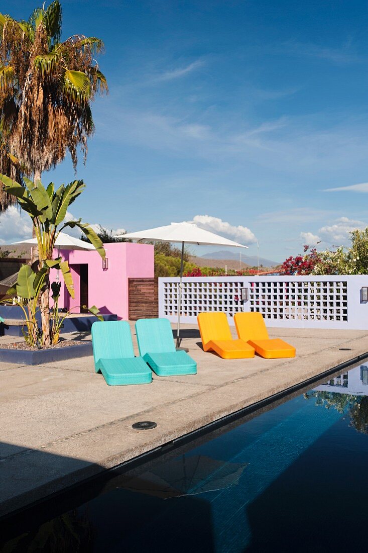 Bunte Liegestühle am Pool, im Hintergrund rosa Bungalow