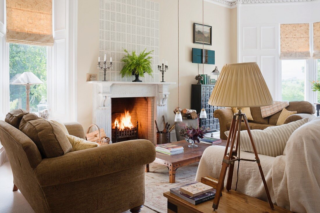 Gemütliches, helles Wohnzimmer mit Couchlandschaft im skandinavischem Stil und brennendem Kaminfeuer; im Vordergrund eine antike Tischlampe