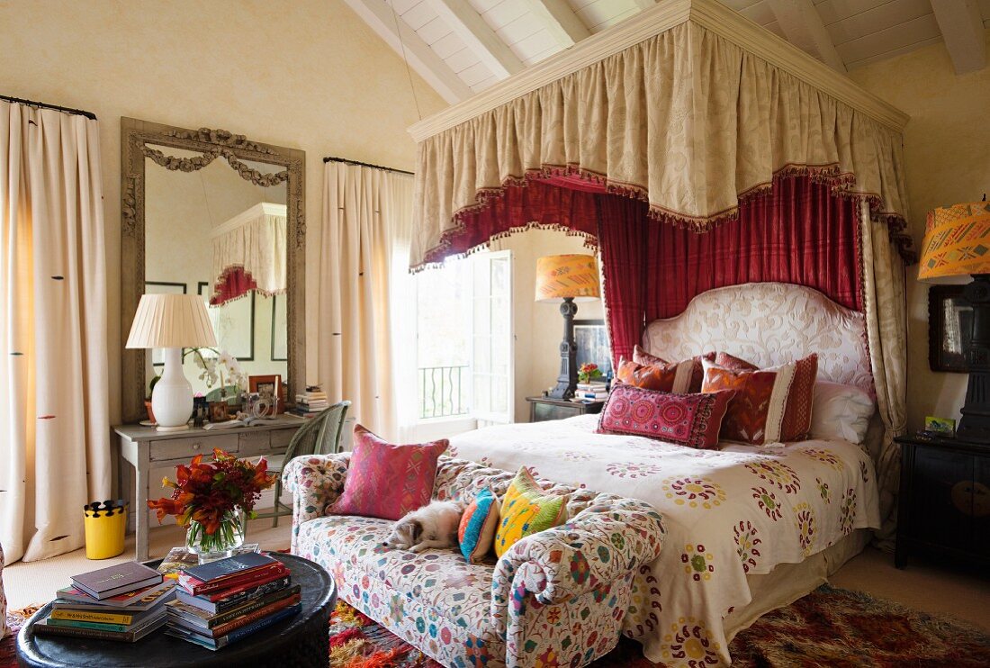 Canopied bed with Marrakech bedding in bedroom with button tufted sofa upholstered in Safi Suzani fabric. Both fabrics designed by Kathryn Ireland