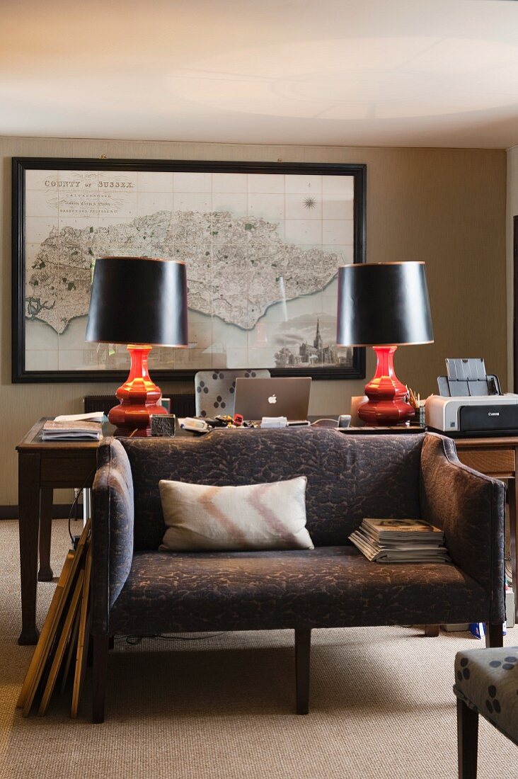 Sofa vor voluminösen Tischlampen beidseits eines kleinen Laptops; Landkarte von Sussex an der Wand
