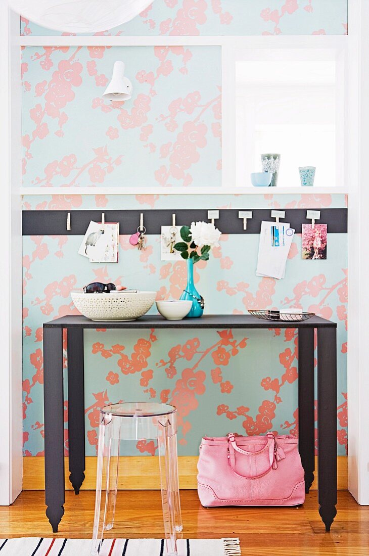 Black, metal console table and transparent, plastic stool against floral wallpaper