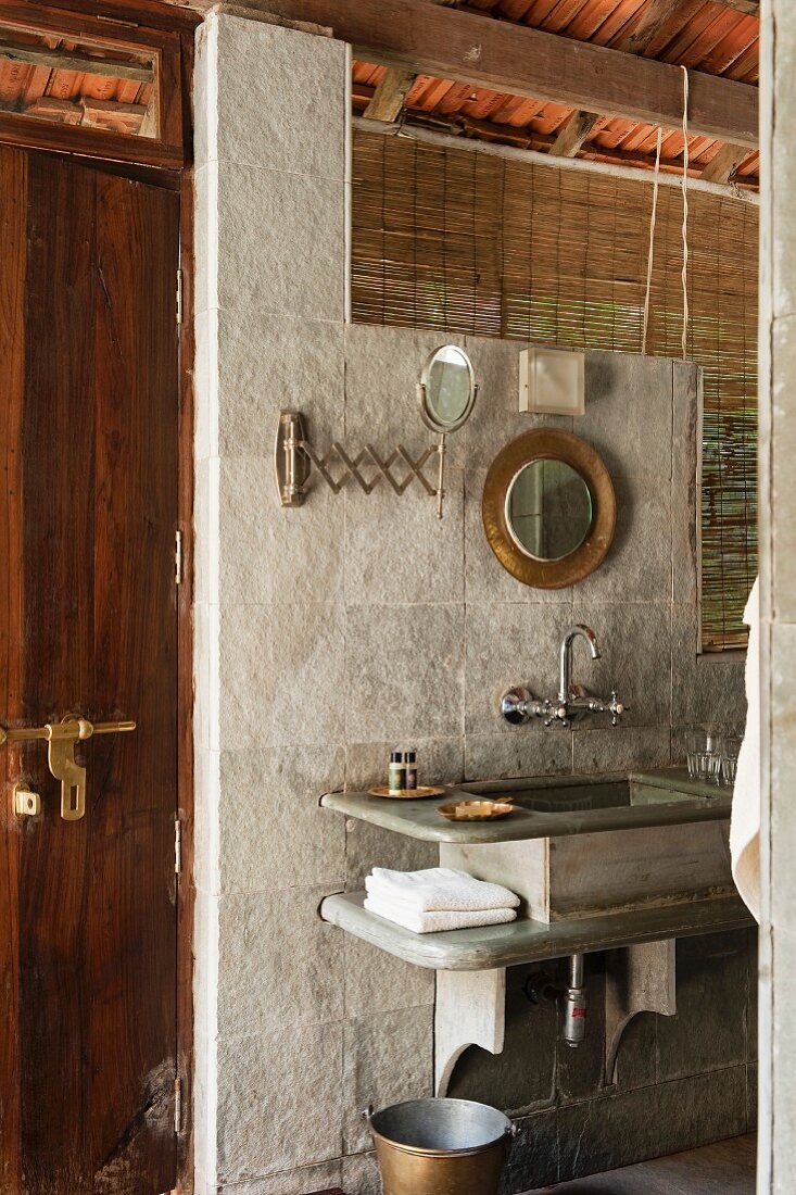 Stone washstand against wall of pale grey stone slabs and bamboo blind at window-like opening