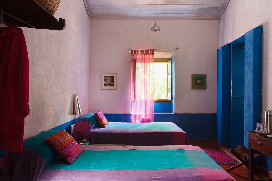 Farbige Tagesdecken in violett und türkis auf Betten in fliederfarbenem Schlafzimmer mit blau getöntem Eingangsbereich