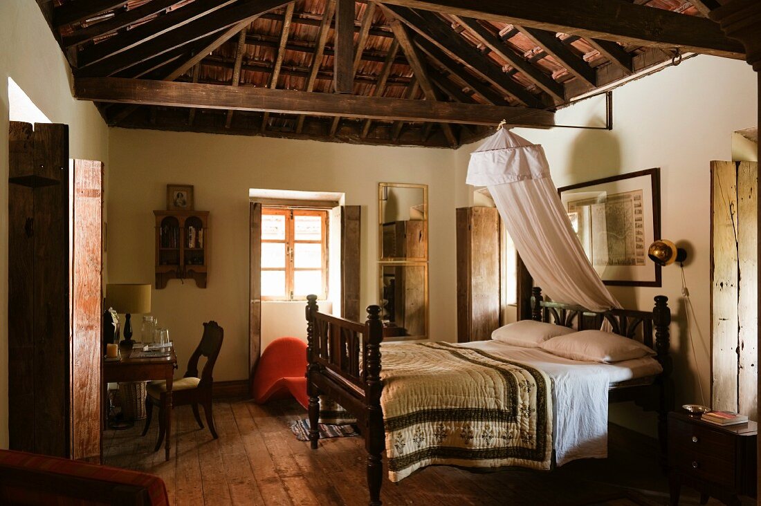 Doppelbett in traditionellem Schlafzimmer eines indischen Wohnhauses mit sichtbarem Dachstuhl aus Holz