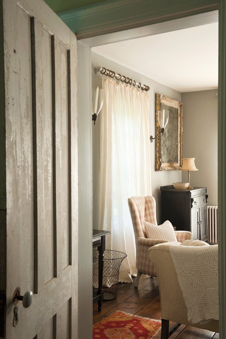 Einblick durch geöffnete Tür in Wohnzimmer im Vintagestil mit gemütlichen Sesseln und Wandkerzenhaltern