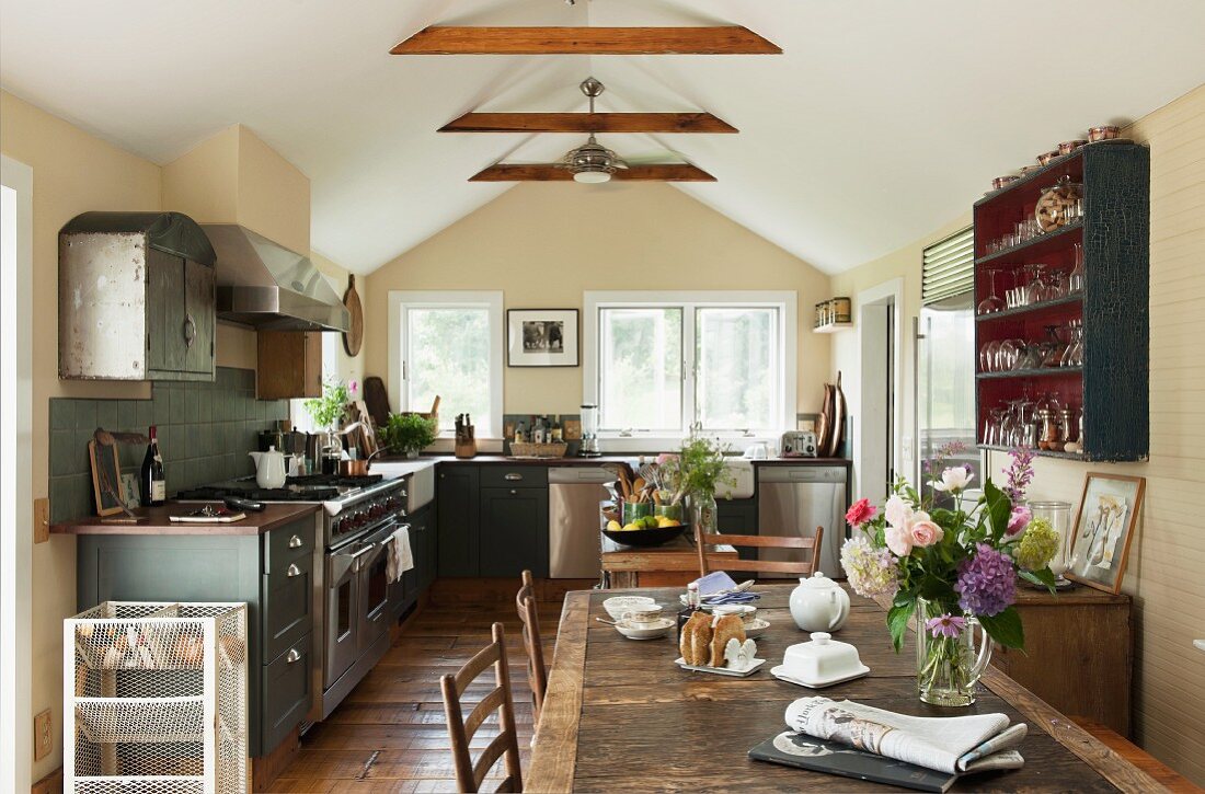 Dachgeschossküche mit Landhausdielenboden und rustikalem Holztisch, dazu eine dunkle Einbauküche