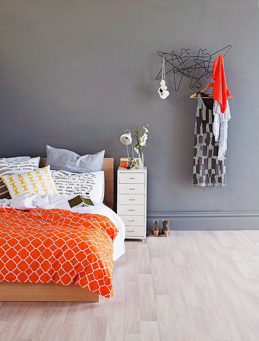 Double bed with modern, colourful bed linen next to dress hanging on clothes rack on grey wall