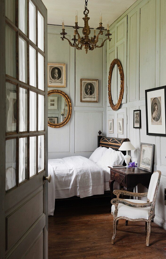 View through open door of bed against grey, wood-panelled walls of traditional bedroom