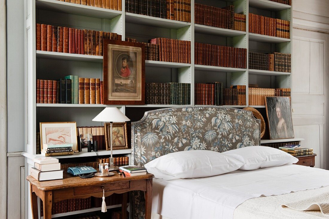 Doppelbett vor offenem Regalschrank mit antiquarischen Bücherbänden