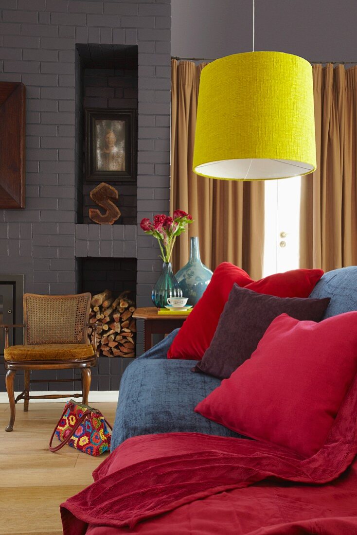 Gemütliche Couch mit roten Kissen und kuscheliger, roter Tagesdecke unter strahlend gelber Hängelampe