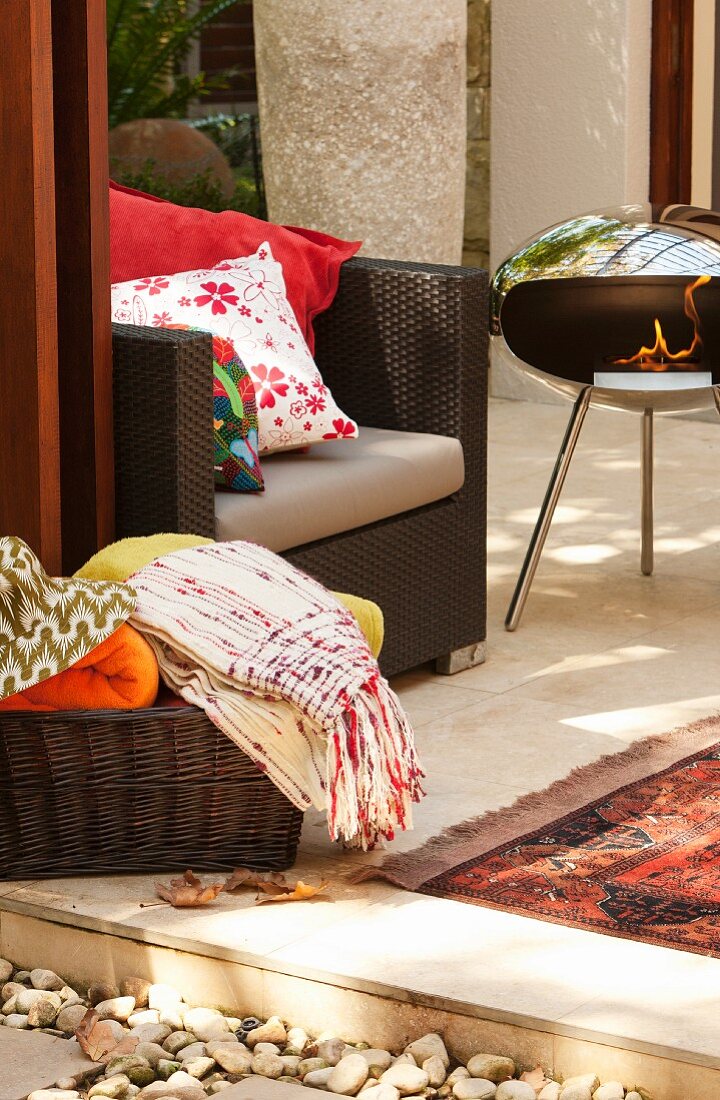 Portable fire bowl, modern outdoor armchair & basket of blankets on veranda