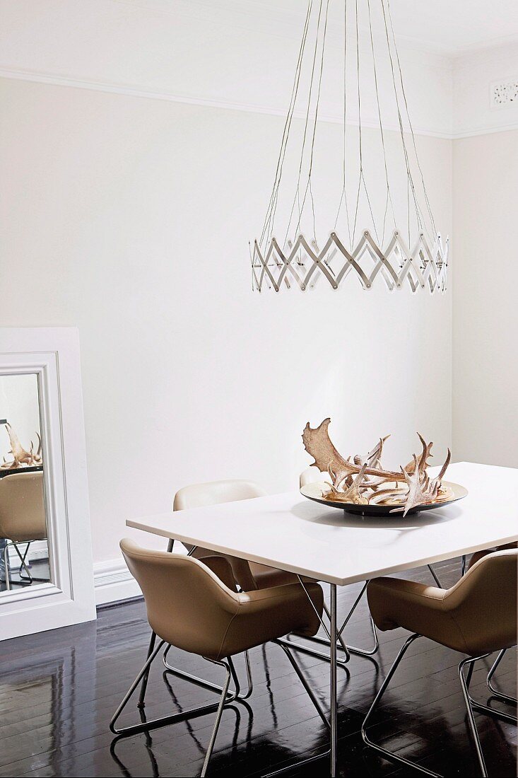 Designer Hängeleuchte über Esstisch mit Hirschgeweih auf Schale und Lederstühle im Fiftiesstil auf dunklem glänzendem Holzboden