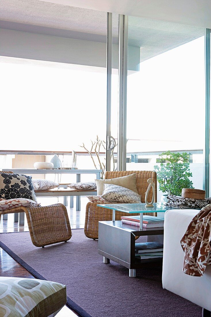 Sitzecke mit modernen Korbsesseln und Couchtisch vor raumhohen Schiebefenster; im Hintergrund einfacher Essplatz auf Terrasse