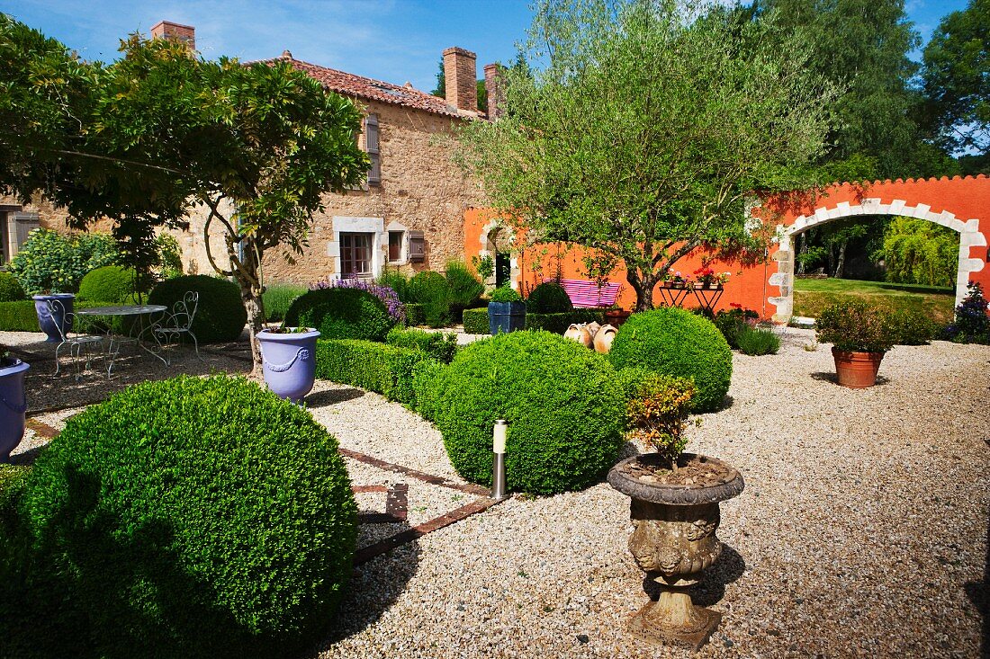 Topiary bushes and planters on gravel in Mediterranean garden of country house villa