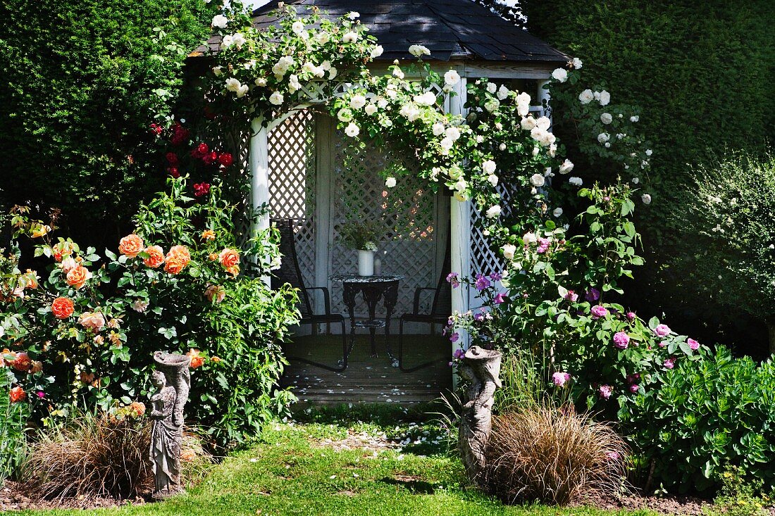 Open summerhouse covered in climbing roses in flowering garden